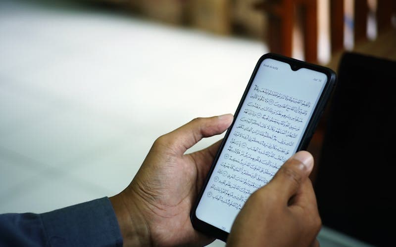 Person reading the Quran on a smartphone